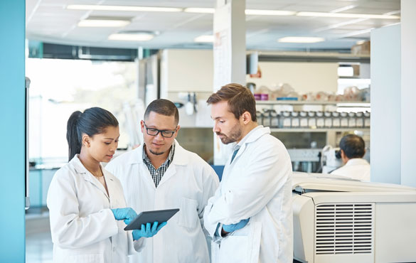 Three technicians stand together and look over data on a clipboard<br>  